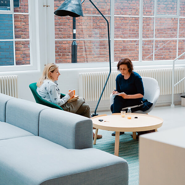Photo of business women sitting in a modern lobby talking over coffee.