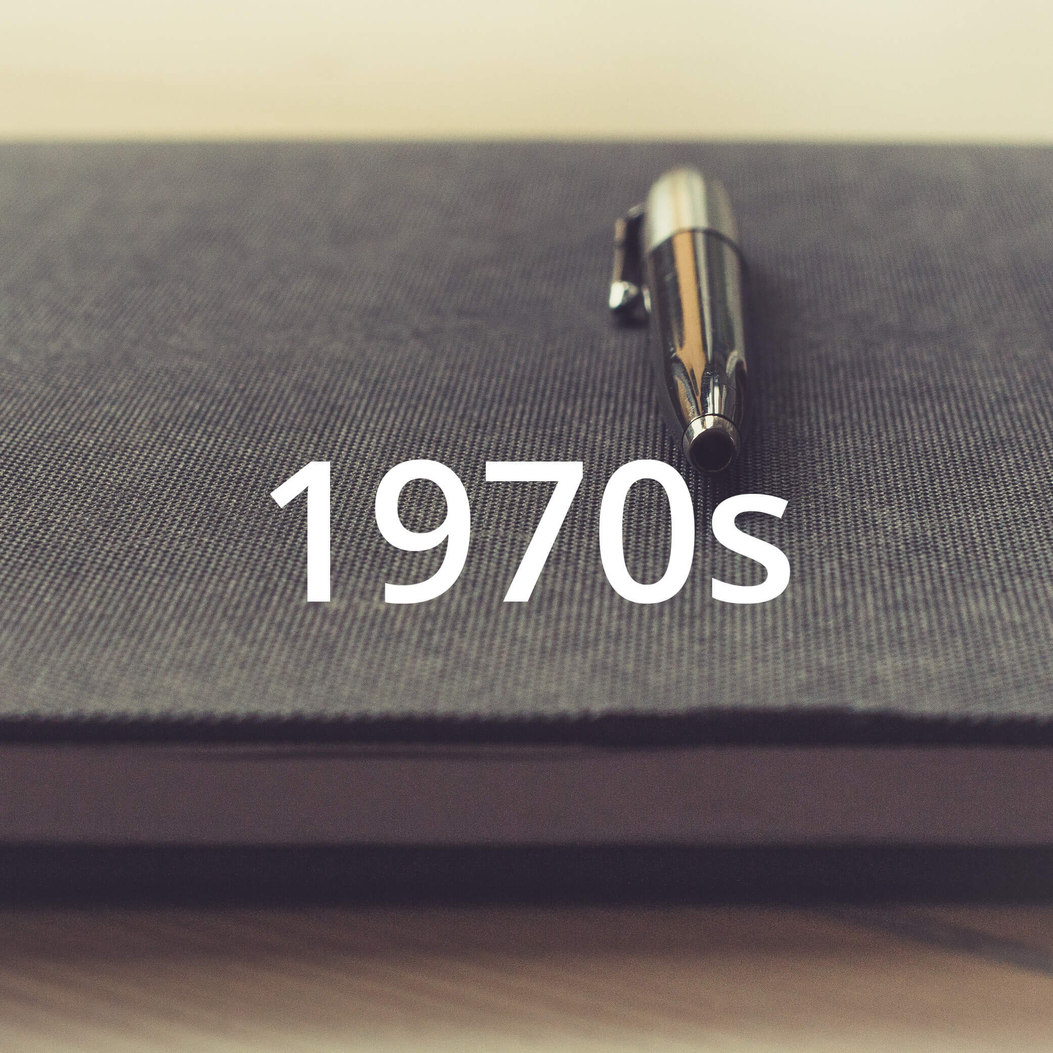 Photo of a pen laying on a book. Photo also features a text overlay that reads "1970s".
